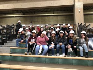 a group of students sit on bleachers wearing white construction hats'