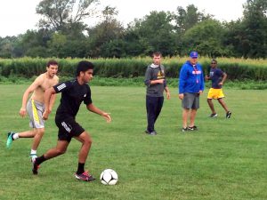 Boys soccer athletes playing in field while two coaches look on