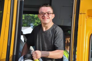 Student getting off of school bus smiles directly at camera