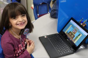 student working at a chromebook pauses for a big smile. The tooth fairy has visited recently.