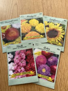 Five packs of seeds sit on a desk. The packages have brightly colored flowers on them.