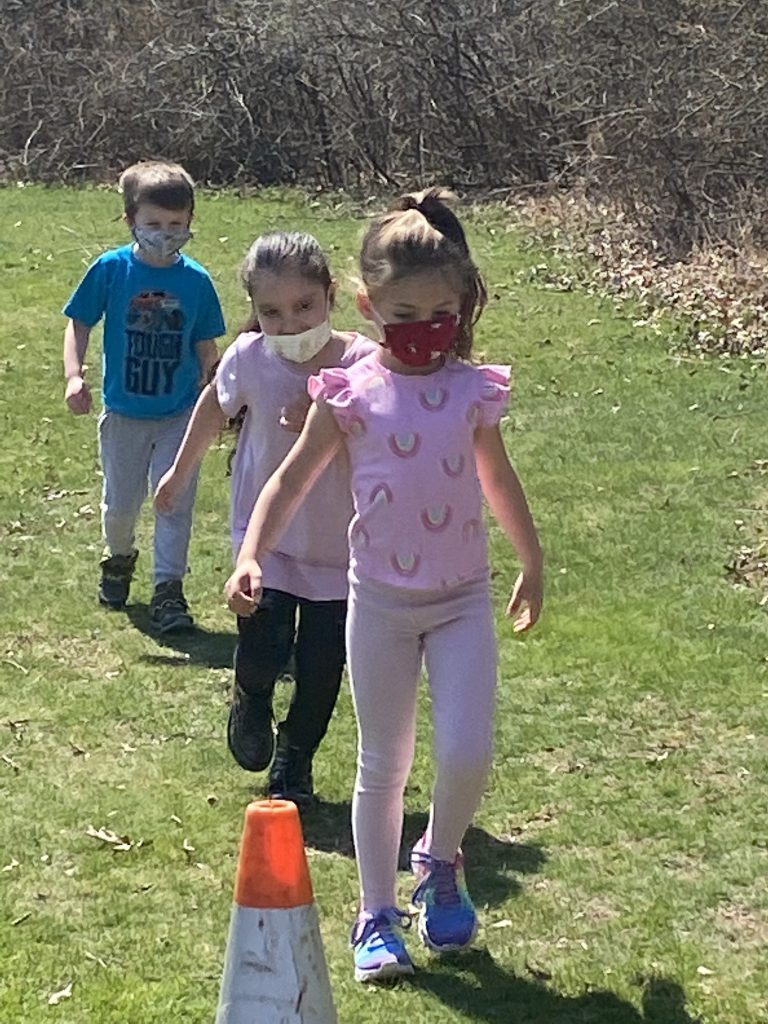 Two elementary school girls and a boy walk in a line. They are wearing short sleeve shirts and masks. 