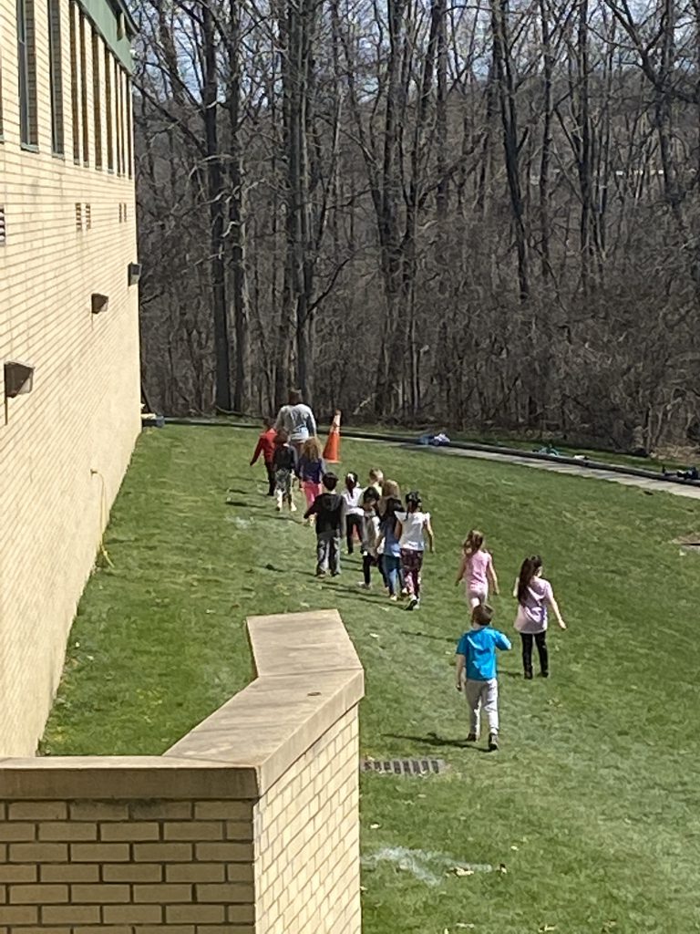 A photo from above where a line of students are walking in the grass with a building on the left.