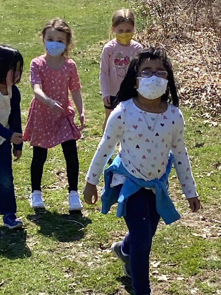 A girl with dark hair and a mask walks in front as three others walk behind.
