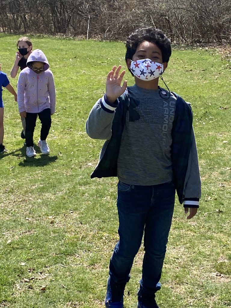 An elementary student wearing a printed mask waves as she walks.