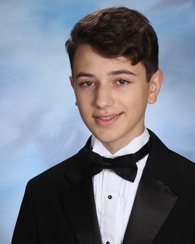 A young man a senior in high school with dark hair smiling. He is wearing a black tuxedo.