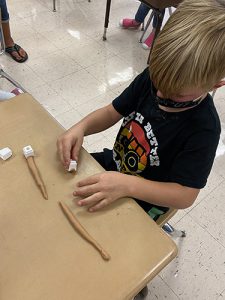 A small boy wearing a black tshirt rolls brown play-doh on a table