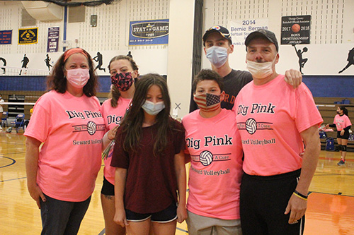 A family of six people stand arm in arm. Four of them are wearing pink tshirts that say Dig Pink for breast cancer awareness. All are wearing masks. There is a woman on the left, a high school girl next to her, a younger girl, a younger boy, an older boy in the backgrond and a man on the right.