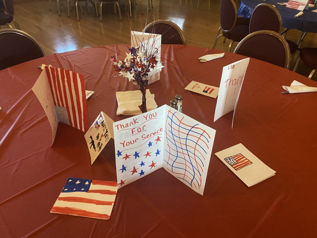 A table with a red tablecloth with handmade patriotic cards set up.