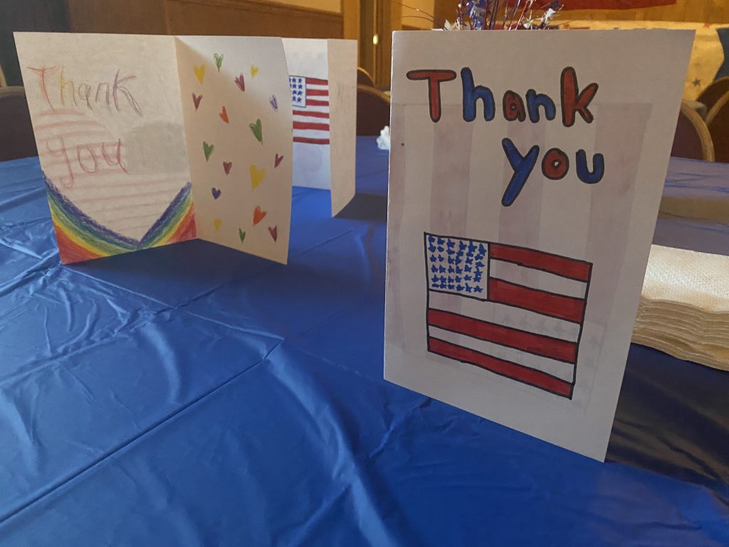 A blue tablecloth with cards set up on it. The one in the front says Thank you with an American flag on it.