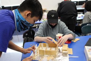 Two high school boys build a gingerbread house.