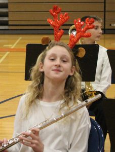 A middle school student with long blonde  hair and wearing red antlers. She has half a smile on her face.
