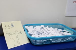 A blue basket filled with white paper cut into snowflakes. Next to it is a sign that says Snow flakes 20 cents