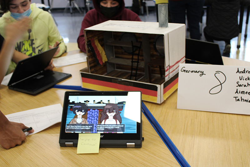 On a table is a diorama of a steerage ship. In front is a Chromebook with information about German immigration.