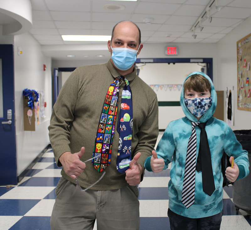 a man on the left and an elementary age boy on the right both wearing two neckties and giving two thumbs up.