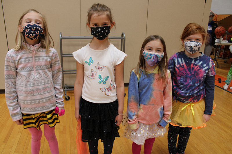 Four elementary-age girls wearing tutus, standing togehter.