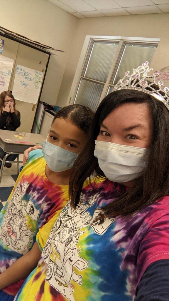 An elementary age girl and a woman both wearing similar tie dye shirts. They both are wearing blue masks as well.