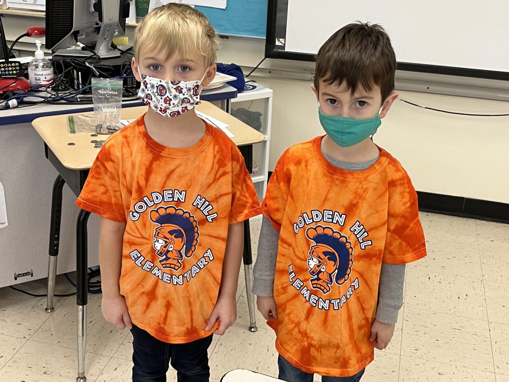 Two elementary age boys wearing orange tie die shirts that say Golden Hill Elementary