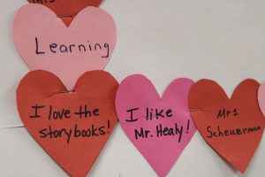 Pink and red paper hearts with messages on them. They say: learning, love the story books, I like Mr. Healey and Mrs. Scheuermann