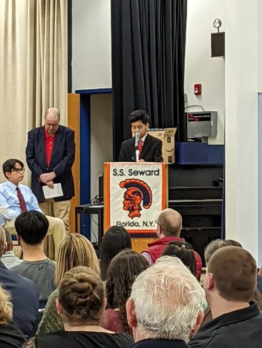 A middle school student stands at a podium and speaks. The podium has a banner that says S.S. Seward Florida N.Y. with a spartan on it.