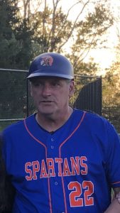 A man wearing a blue baseball helmet, blue baseball jersey that says SPARTANS on it in orange.