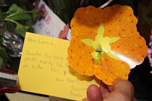 An orange paper flower with a yellow center. There is a note attached saying Mrs. Lysack, Thanks for being a great nurse. You help a lot of kids this year. Your Fried Jameson .