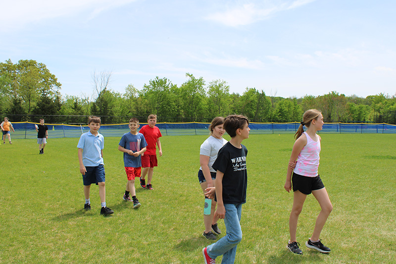 A group of six older elementary school kids walking on a field of grass.