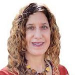 A headshot of a woman with longer curly hair smiles. She is wearing an orange shirt and large chunky necklace.