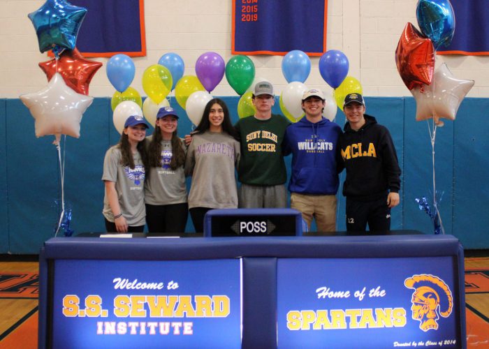 Six people stand behind a table with SS. Seward Institute Home of the Spartans on the cover with photos behind them.