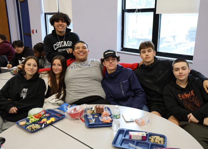 Students pose for a photo around a lunch table