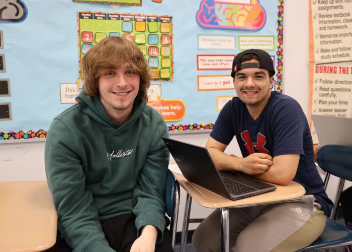 Two students pose near a desk