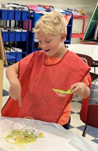 A student in a red smoke creates bubbles on a table