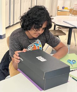 A student works on a project using a shoebox