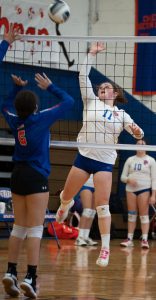 A volleyball player jump to hit a ball behind a net as a player attempts to defend.