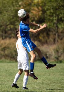 A soccer player heads the ball while jumping into another player.