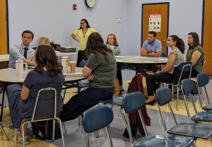 People sit at round tables in a room as a person speaks