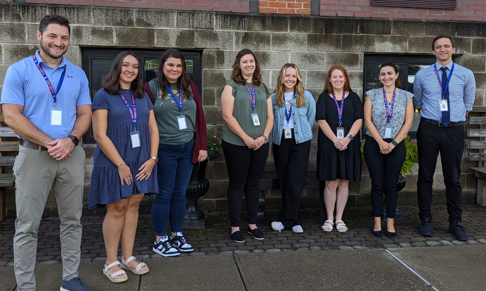 Teachers pose for a photo in front of a concreate brick wall.