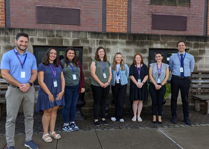 Teachers stand pose for a photo in front of a concrete wall.