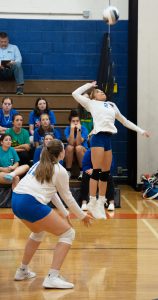 A volleyball player jumps to hit a ball as another crouches.