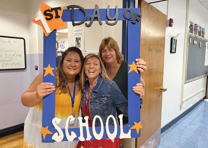 Three people pose with a first day of school frame