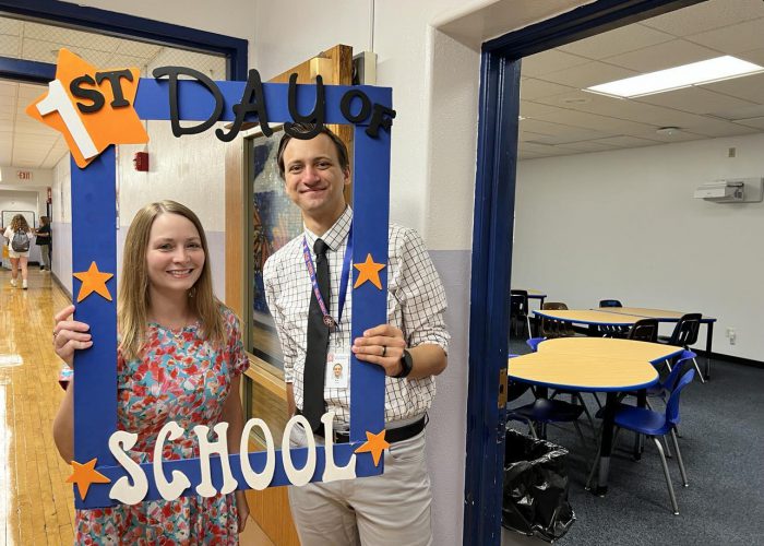 Two people pose with a first day of school frame