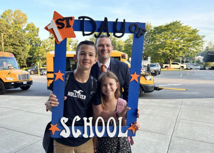 Three people Two students pose with a first day of school frame