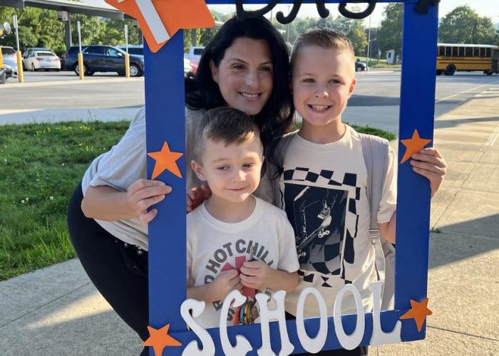 Three people pose inside a First day of School frame