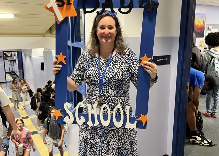 A person poses with a first day of school frame