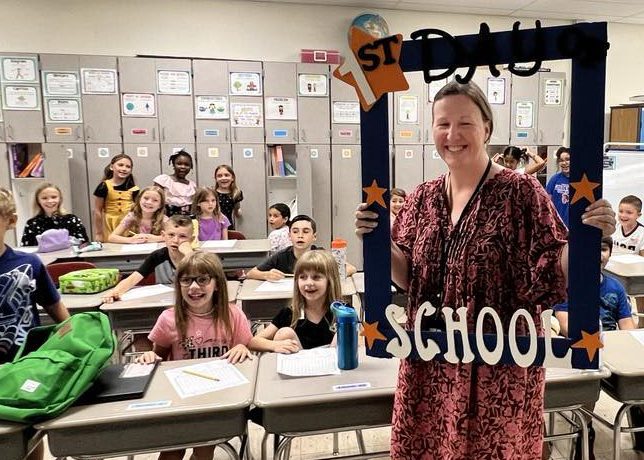 A teacher holds a First Day of School frame with her class around her