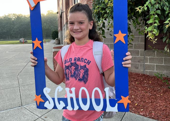 A student poses with a first day of school frame