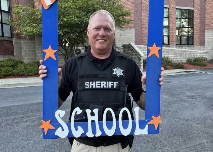 A law enforcement officers poses with a first day of school frame