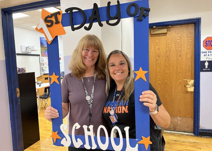 Two people pose with a first day of school frame