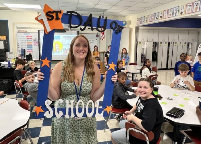 A teacher holds a First Day of School frame with her class around her
