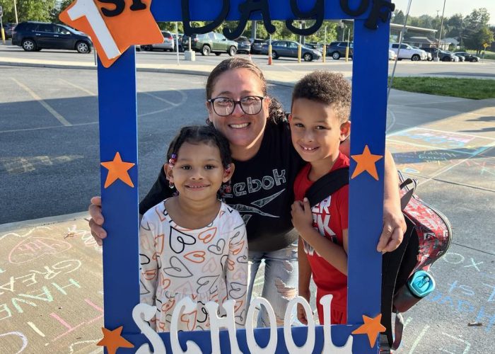 Three people hold a first day of school frame